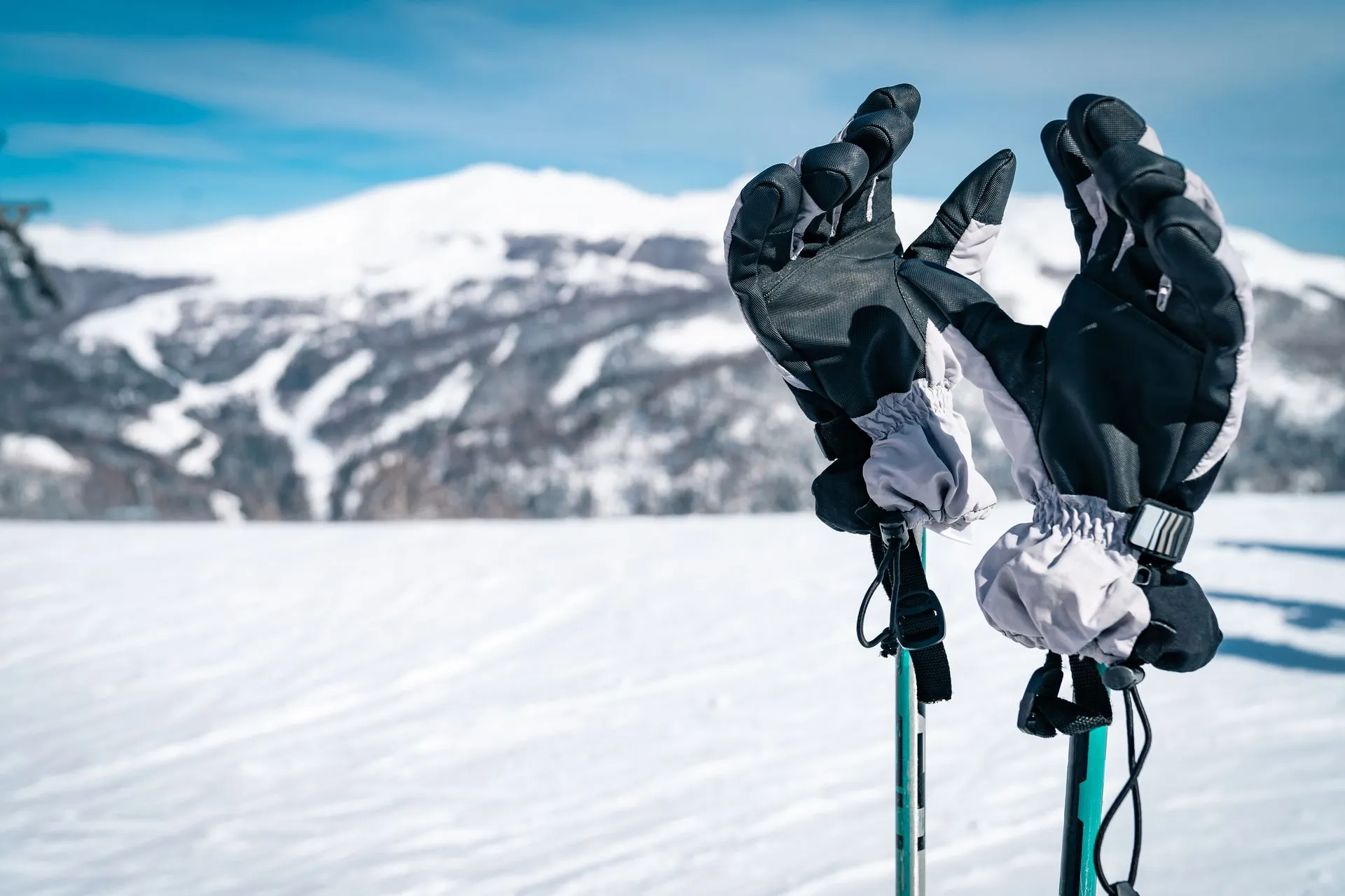 Skihandschuhe auf Skistöcken vor einer verschneiten Piste und sonnigem Bergpanorama